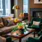 Living room with a brown sectional sofa, green armchairs, and a coffee table with flowers.