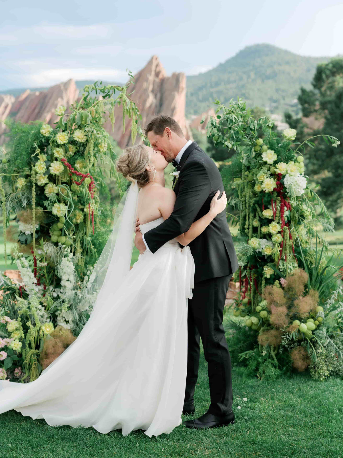Couple sharing a kiss at a wedding with floral arches in littleton arrowhead golf course Colorado