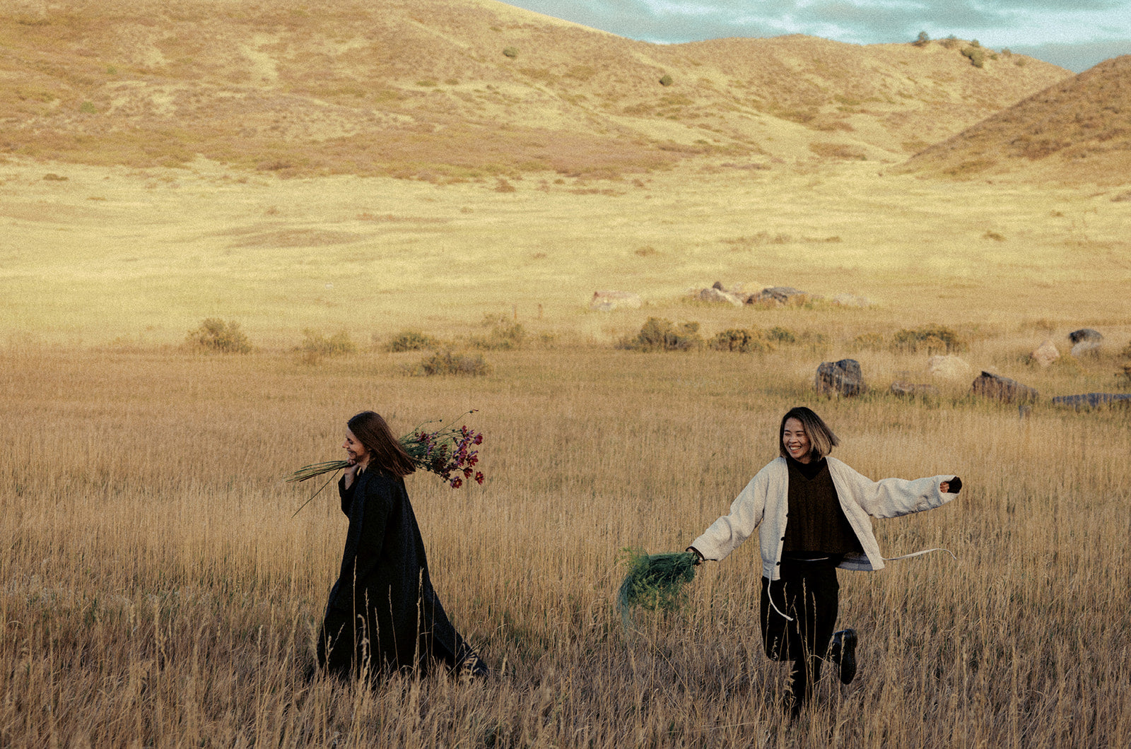 Two women walking through a field with hills in the background. Photoshoot for Skyler and Dasha. Shaa.Project