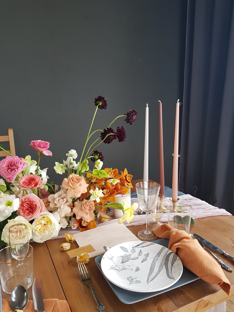 Dining table setting with flowers, candles, and cutlery against a dark background
