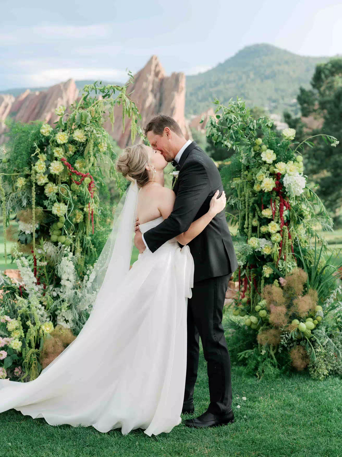 Bride and groom kissing under lush green wedding floral arch at Arrowhead Golf Course, Colorado wedding ceremony