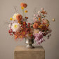 Floral arrangement in a silver vase on a concrete pedestal against a beige background