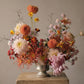 Floral arrangement in a silver vase on a stone pedestal against a plain background