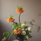 Artful seasonal flower arrangement with orange fritillaria, greenery, and sculptural stems
