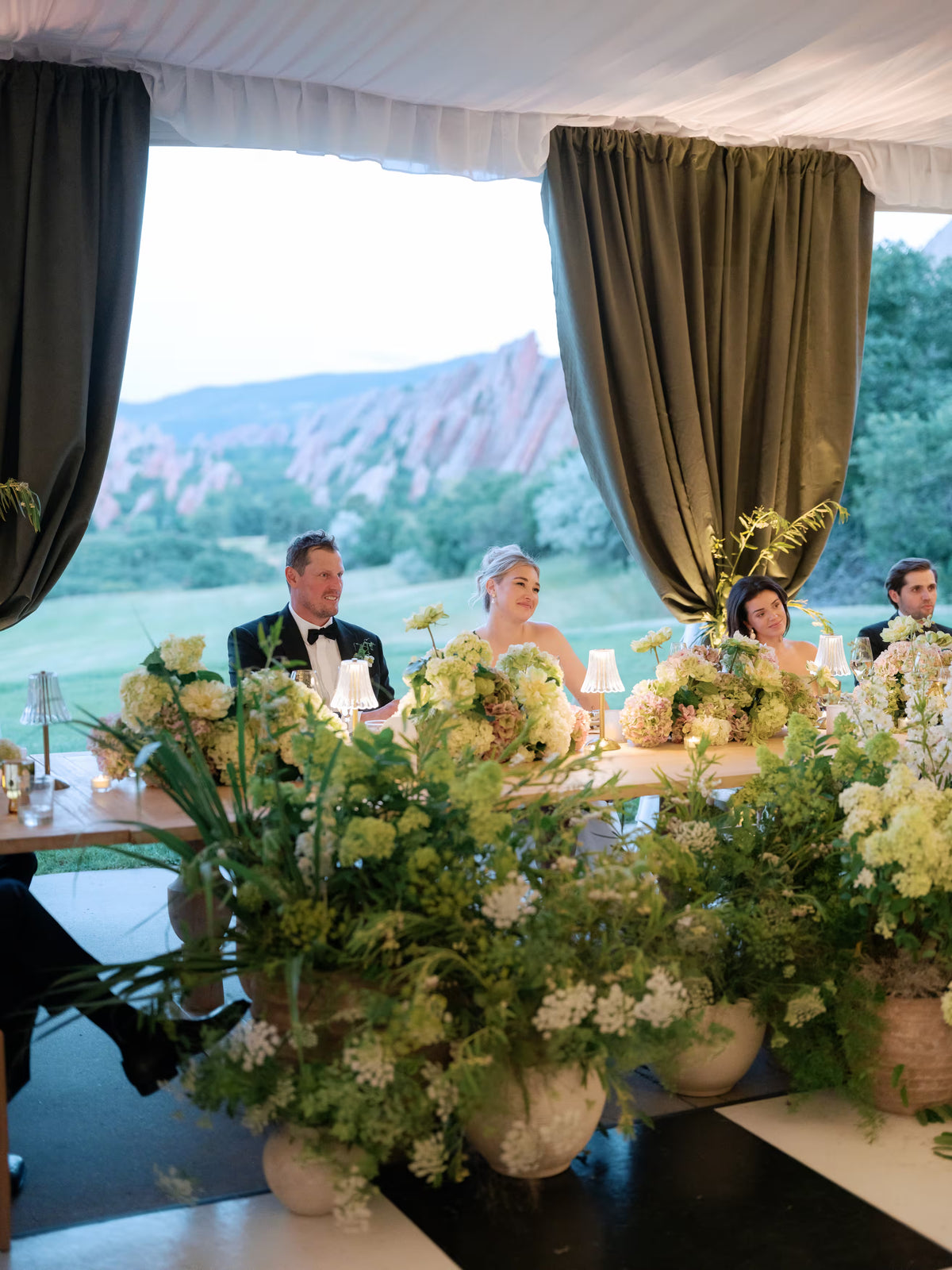 Wedding reception with couple seated at long table surrounded by lush floral arrangements at Denver Colorado venue