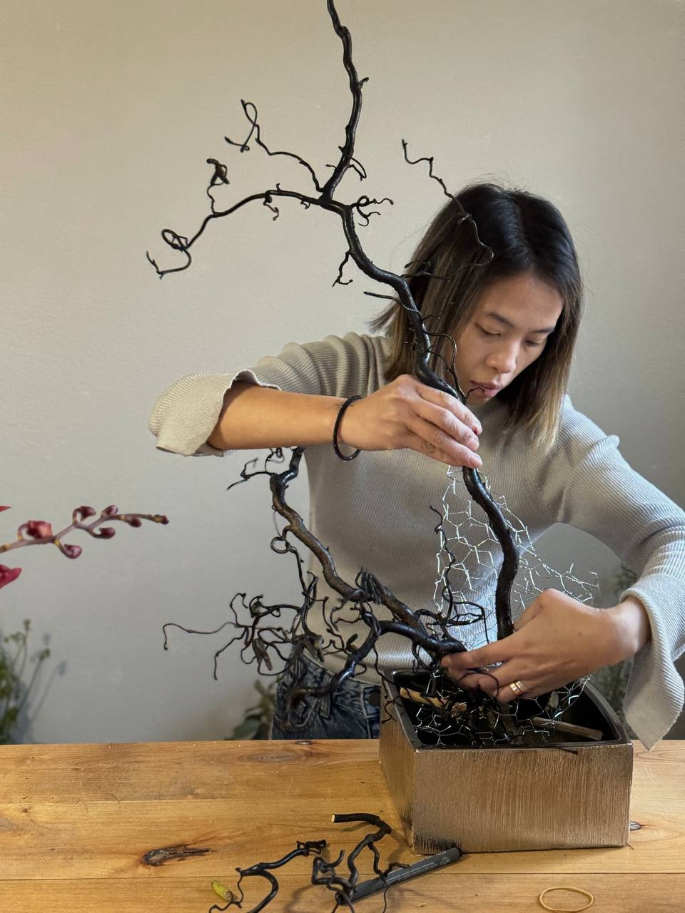Floral designer creating Red Noir sculptural arrangement with branches and red flowers