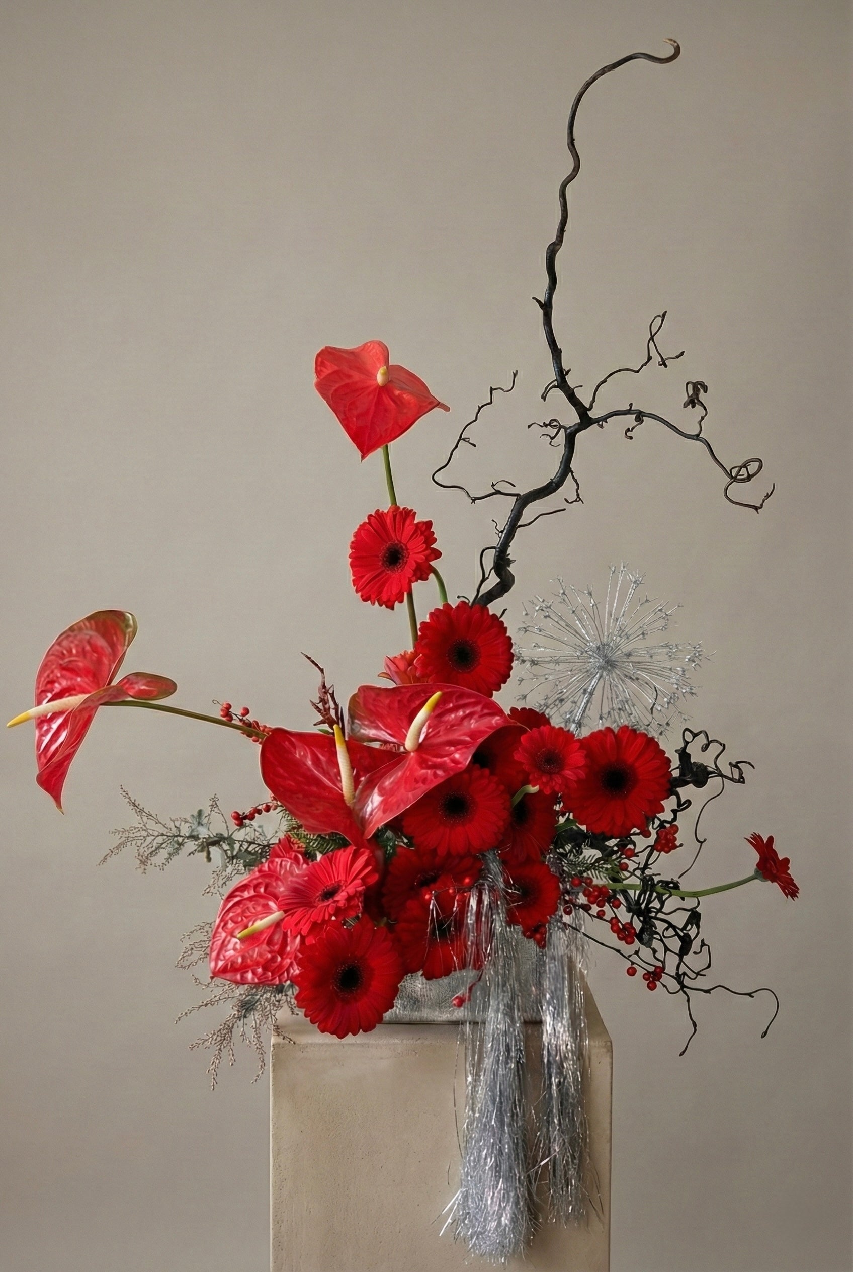 Abstract Floral arrangement with red flowers and black branches in a clear vase against a beige background