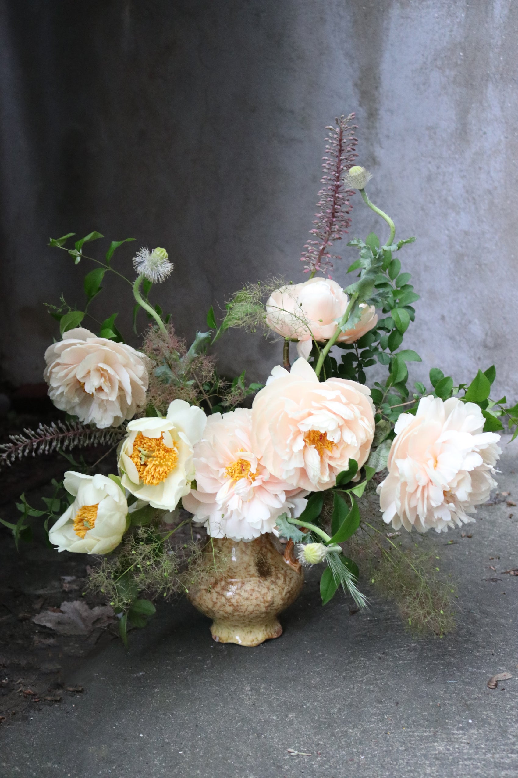 Floral arrangement with peach and white flowers in a textured vase on a concrete surface.