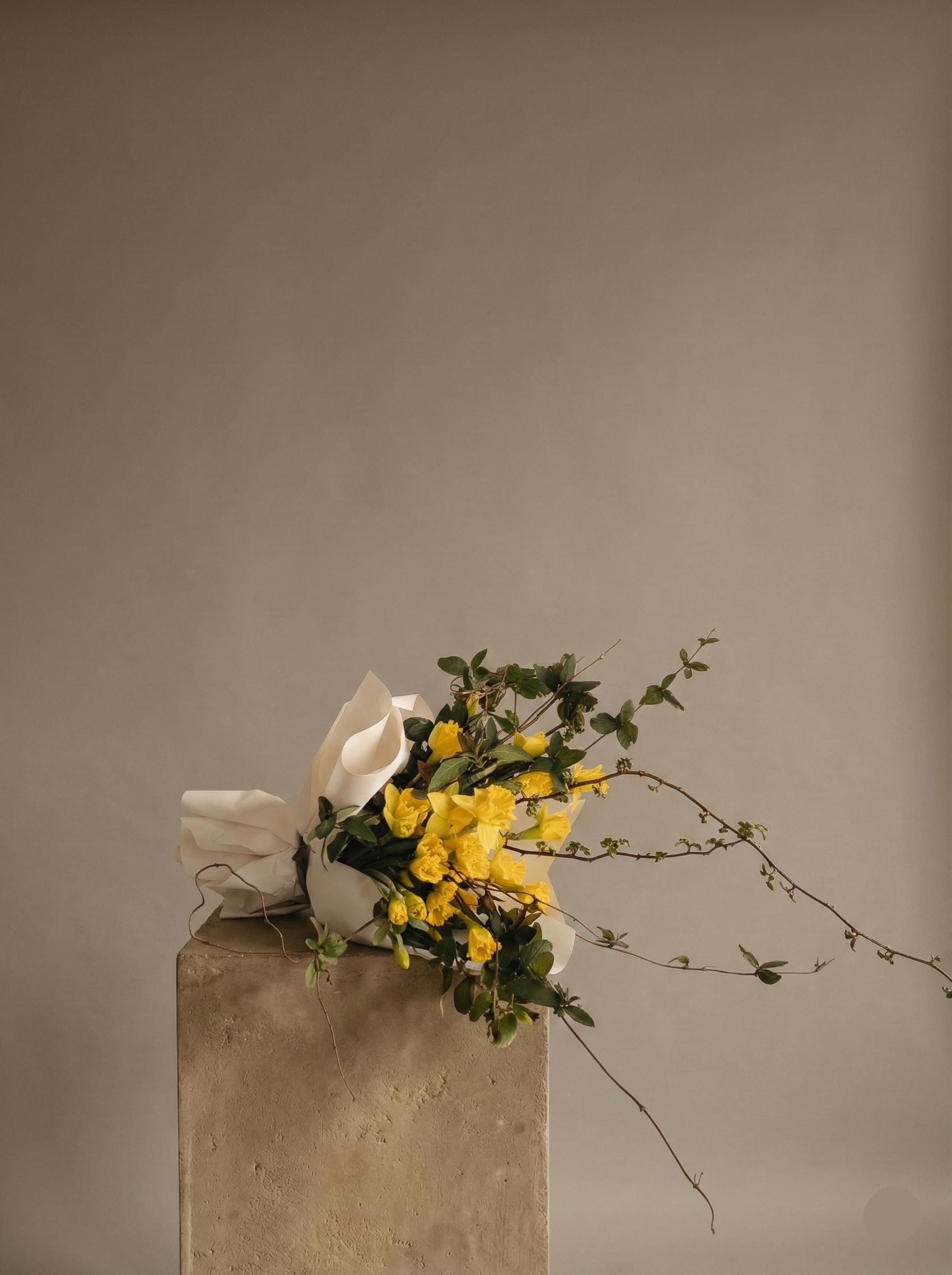 Bouquet of yellow flowers and white paper on a concrete block against a beige background