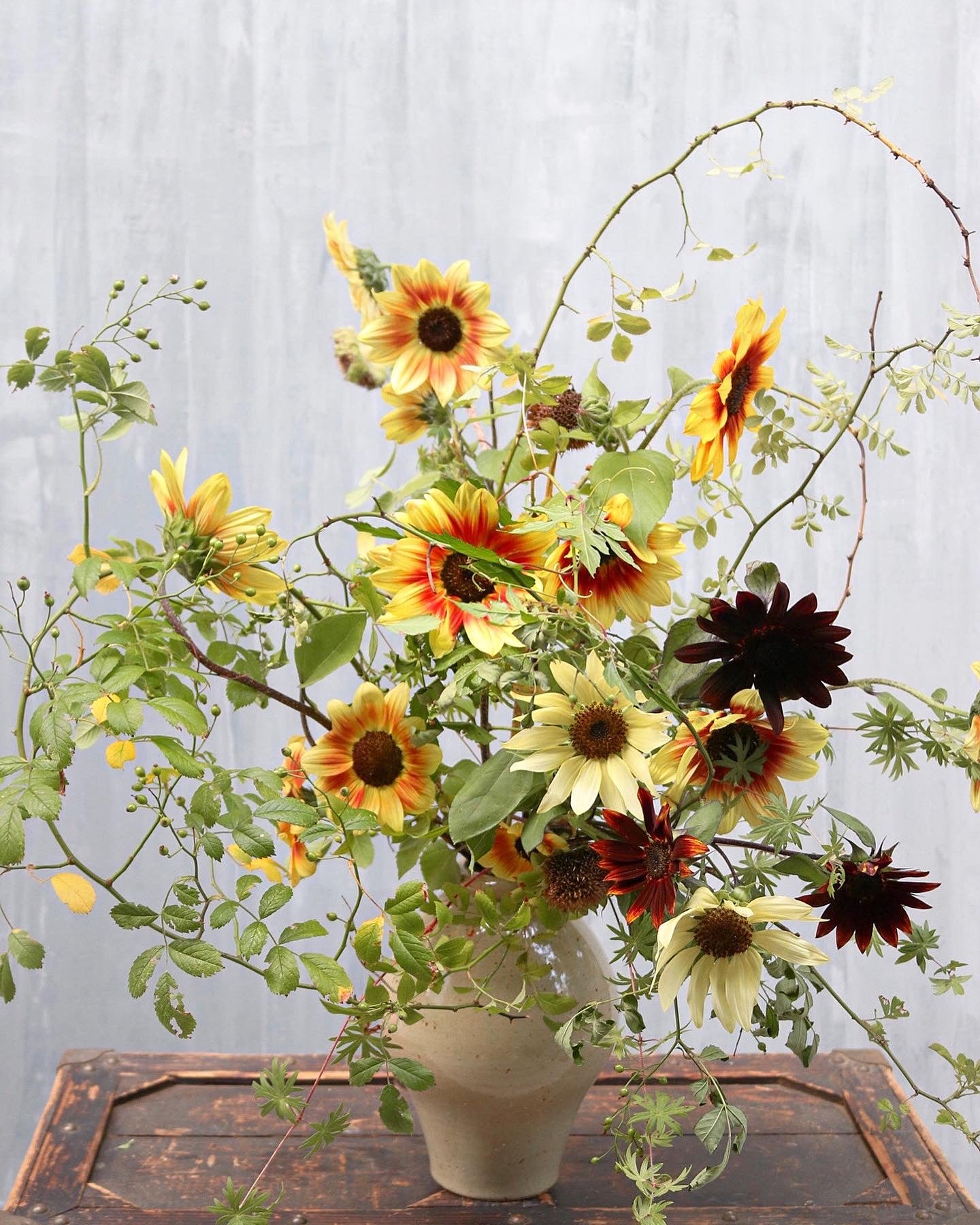 Floral arrangement with sunflowers and greenery in a vase on a wooden surface.