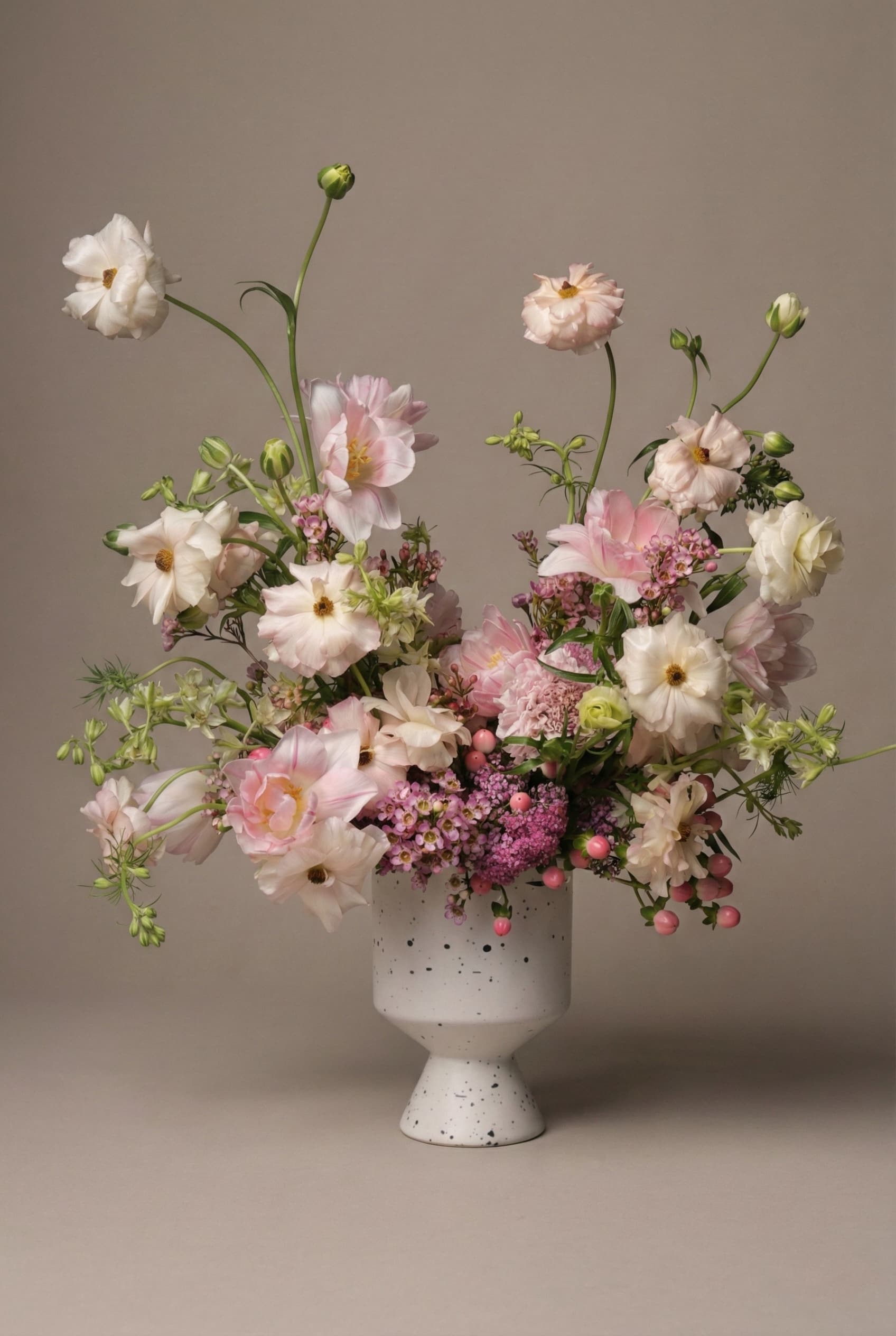 Soft pink garden-style flower arrangement with cosmos, ranunculus, and seasonal blooms in a speckled ceramic vase