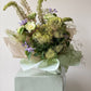 Bouquet of green and purple flowers wrapped in brown and green paper with a white ribbon 