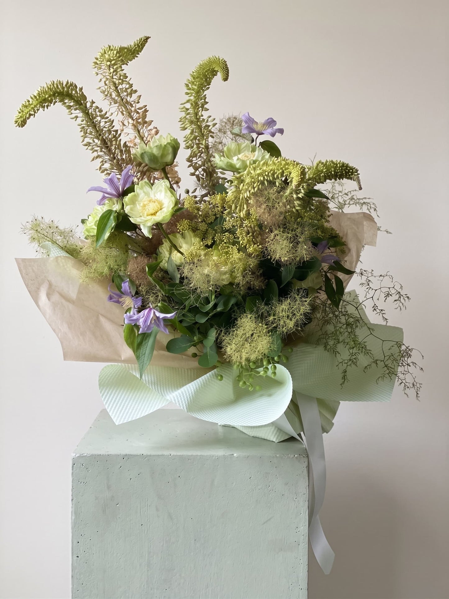 Bouquet of green and purple flowers wrapped in brown and green paper with a white ribbon 
