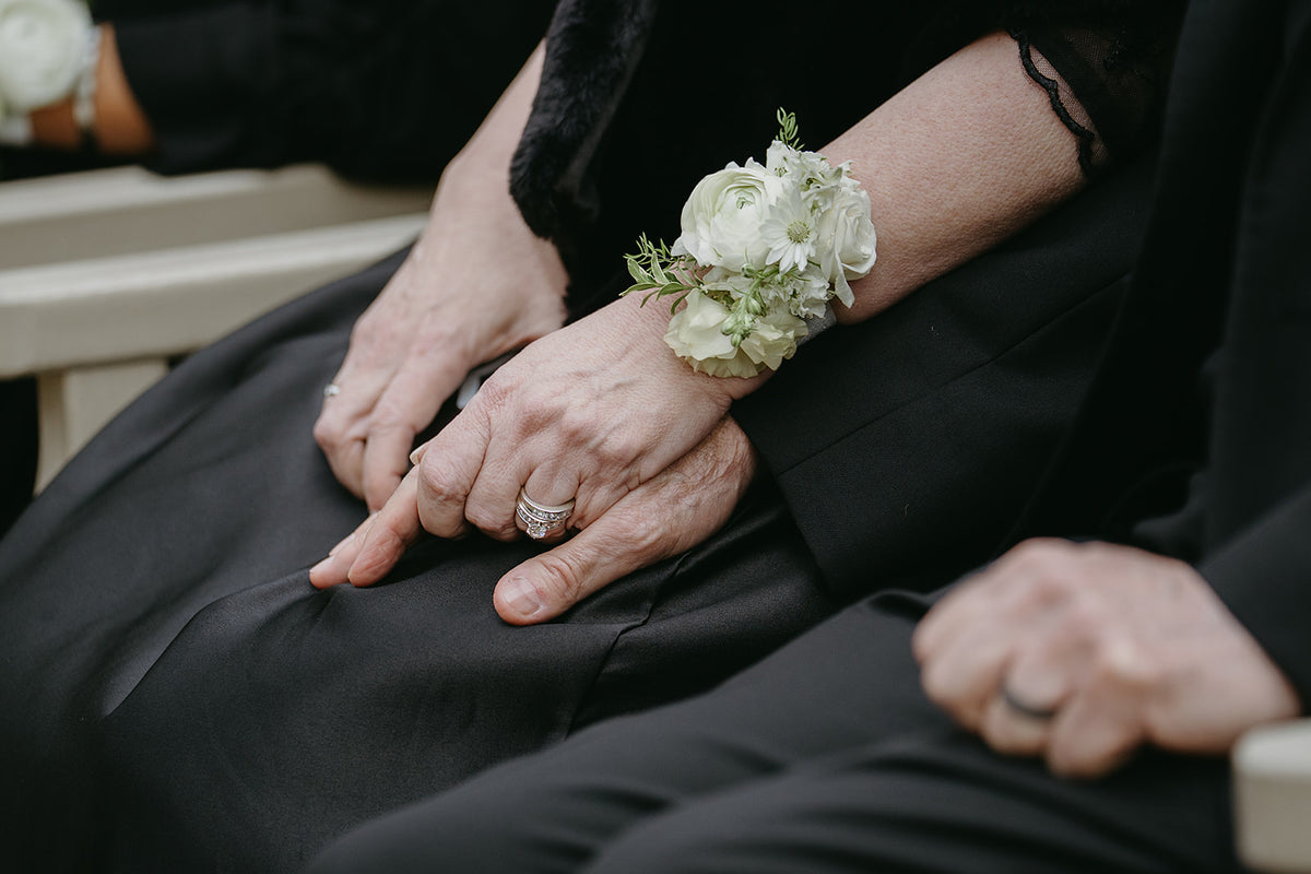 Close-up of hands with wedding rings and floral wrist corsages 